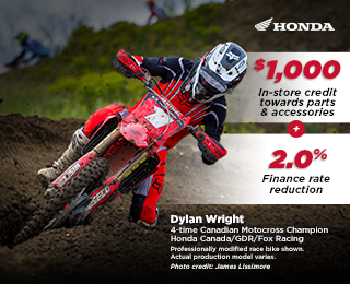 A Honda racer on his bike on a track, raising his arms in victory. Photo credit to James Lissimore.