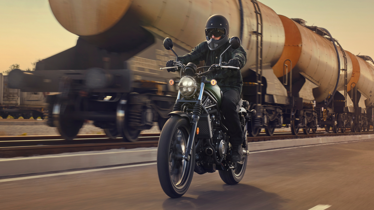 A Honda Standard motorcycle being ridden beside a train 