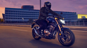 A rider on a Honda Standard motorcycle at dusk with pink clouds in the background