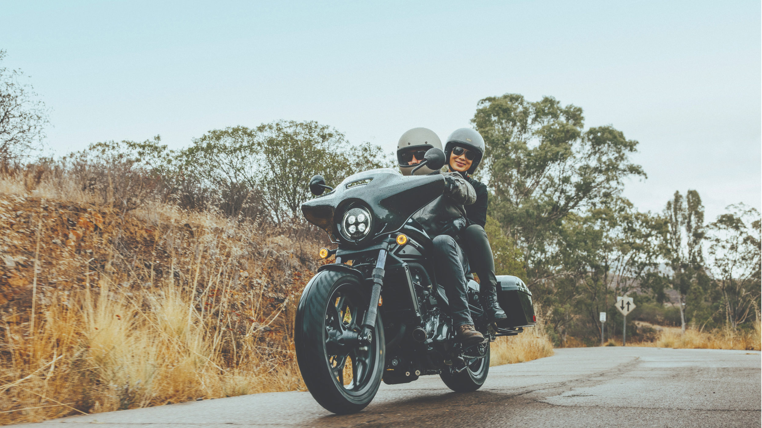 Two riders on a Honda Rebel on a road with yellow grass growing on the side of the road