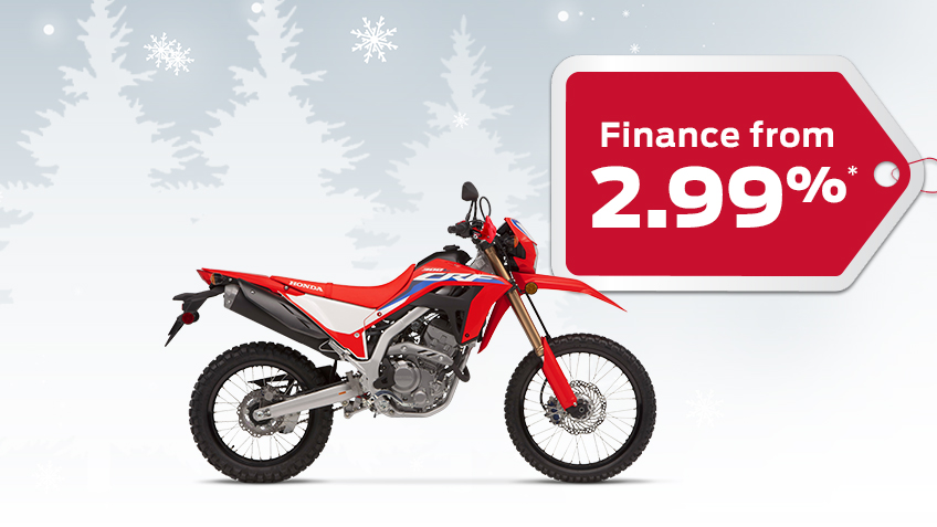 A Honda CRF300L on a winter backgroud with snowflakes with a red gift tag advertising a 2.99% interest rate 